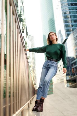 Uzun boylu, kısa sarı saçlı, mavi pantolonlu, botlu, kaba sokak duvarına karşı poz veren, minimalist şehir tarzı giyinen hippi bir kız..
