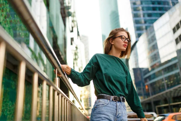 短い髪型でヒップスターの女の子の肖像画は 側の都市の通りにポーズを見て 近代的な建物の背景にあります 水平方向 — ストック写真