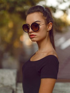 Siyah ince elbiseli, güneş gözlüklü, at kuyruklu güzel esmer bir kızın yakın plan ön portresi..