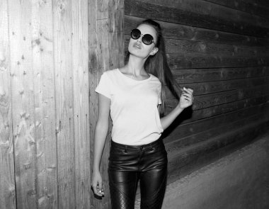 Akşamları tahta duvarın yanında poz veren çekici beyaz bir kadının siyah ve beyaz görüntüsü..
