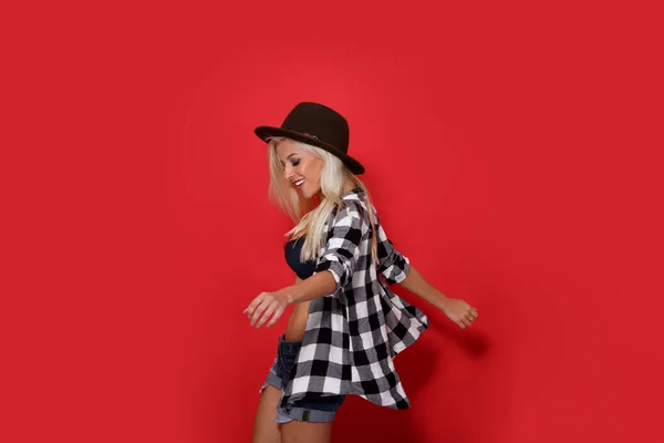 フロントポートレートの若いですヒップスターとともにセクシー運動体身に着けている帽子 ダンスでスタジオ 隔離された赤の背景 — ストック写真