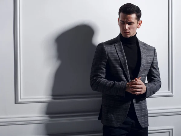 Bonito, jovem sério posando no estúdio perto da parede branca em terno elegantemente cinza, sombra. Conceito de homem de negócios. — Fotografia de Stock