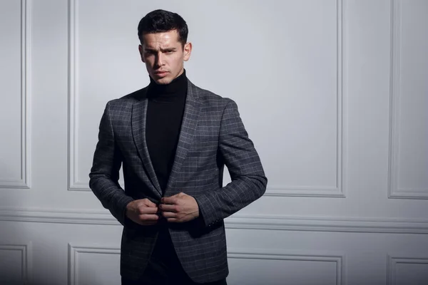 Sério retrato de um homem de terno preto-cinza, posando elegante perto da parede branca em estúdio, isolado em fundo branco. — Fotografia de Stock