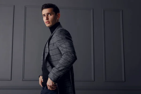 Un hombre con una chaqueta gris chal y cuello alto, de perfil con las manos en los bolsillos y mirando confiado. —  Fotos de Stock