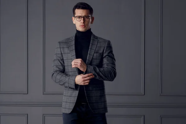 Empresario confiado usar traje gris con estilo y gafas negras se ve con actitud, sobre fondo de pared gris. — Foto de Stock