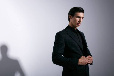 Siyah takım elbiseli, vahşi bir gencin yakışıklı portresi. Profilde kameraya bakıyor. Stüdyoda duruyor..