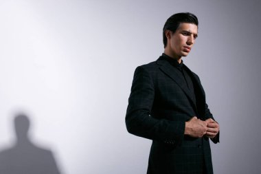 Genç bir adamın portresi stüdyoda tavır takınıyor, takım elbisesini ayarlıyor, beyaz arka planda izole edilmiş..