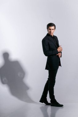 Kendine güveni tam bir adam, beyaz bir arka planda izole edilmiş, tutumuyla poz veriyor. Kapalı alanda dikey çekim.