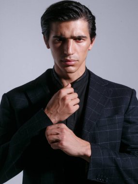 Siyah takım elbiseli esmer adamın portresi, ceketinin düğmelerini düzenledi, stüdyoda tavır takınarak poz verdi, beyaz arka planda izole edildi..