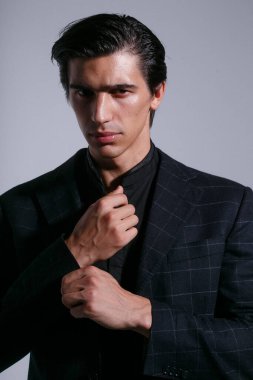 Siyah takım elbiseli esmer adamın ön portresi, ceketinin düğmelerini düzenledi, stüdyoda tavır takınarak poz verdi, beyaz arka planda izole edildi. Dikey görünüm.