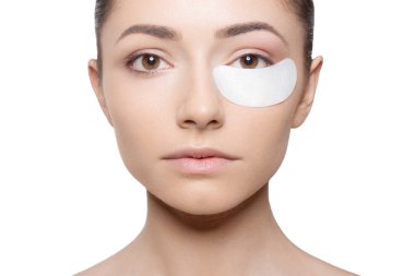 Makyaj sırasında gözünün altına sıva süren kameraya bakan kadının yüzü..