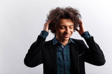 Kıvırcık saçlı genç adam gülüyor ve elleriyle saçlarına dokunuyor, beyaz arka plan, mesaj için boşluk..