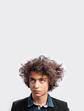 Harika saçı olan, kulaklıklı, dalgın görünen, beyaz arka planda soyutlanmış şüpheli bir genç. Dikey görünüm.