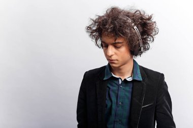 Yatay görüş. Umutsuz, kıvırcık saçlı, kulaklıklı, dalgın, beyaz arka planda soyutlanmış bir genç portresi..