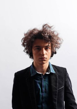 Saçları harika, kulaklıklı, dalgın, beyaz arka planda izole bir şekilde duran şüpheli bir gencin portresi. Dikey görünüm.