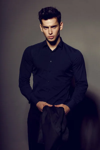 Portrait of rich, sexy brunette man in black suit posing on camera, isolated on grey background. — Stock Photo, Image