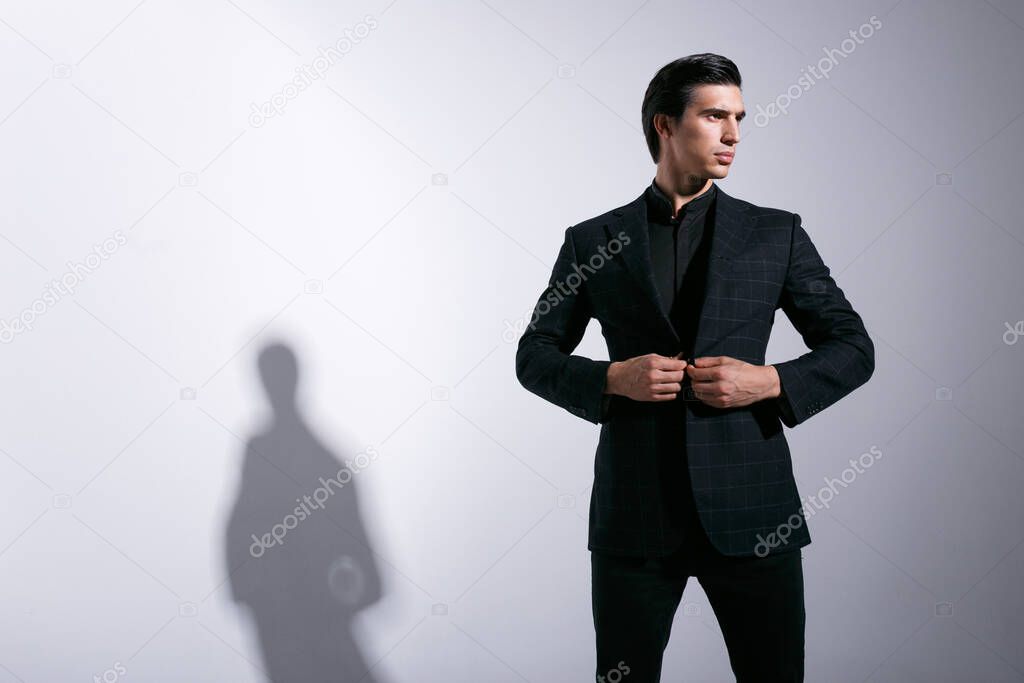 stylish brunette man in a stylish suit, holding hands on checkers jacket, isolated on white background. Horizontal indoors
