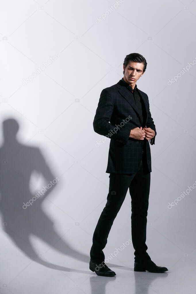 Young man poses in studio with attitudine, looking at camera, adjusting his suit, isolated on white background.