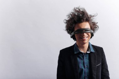 Harika kıvırcık saçlı, gülümseyen, aptal bir gencin portresi, gözlerine kulaklık takan, beyaz arka planda müzik dinleyen. Metin için boşluk.