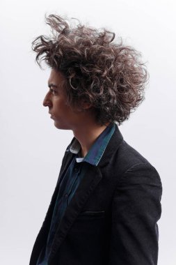 Kaşlarını çatmış genç bir adamın portresi, dağınık bir saç stili, montunu giyiyor, dikiliyor, başka tarafa bakıyor, beyaz arka planda soyutlanıyor. Kopyalama alanı ile dikey görünüm.