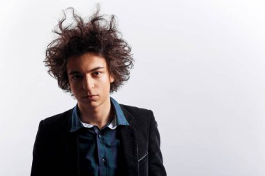 Yatay görüş. Kıvırcık saçlı, bakımsız, üzgün bir gencin portresi beyaz arka planda gömlek ve ceket giymiş kameraya bakıyor..