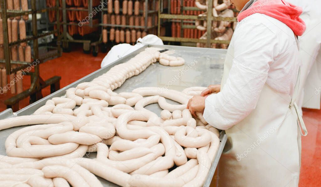 A worker prepares sausages on a table at a meat processing factory, food industry.