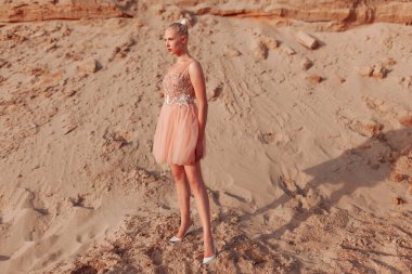 Çölde nakış işleyerek poz veren, kumların üzerinde duran sarışın güzel bir kadın resmi..