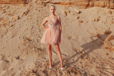 Çölde poz veren, nakış işlemeli elbiseli çekici sarışın bir kadın resmi..