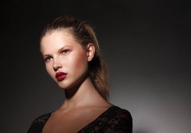 Saçları at kuyruklu, koyu gri arka planda güzel sarışın bir genç kızın profil portresi..