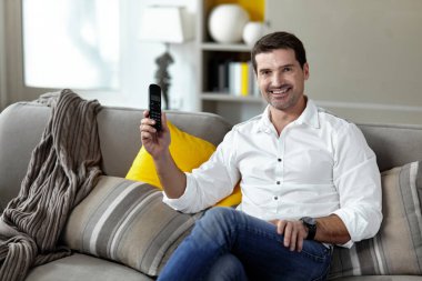 Neşeli bir gencin ön portresi kanepede oturmuş elinde sabit bir telefonla kameraya bakıyor..