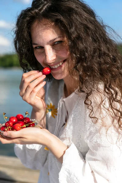 Close up photo of cheerful funny cute nice sweet curly girl with lips pomaded holding a cherry with hand, outside portrait. — Stock Photo, Image