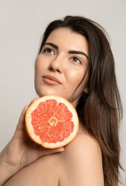 Güzel, yarı çıplak, makyajsız bir kadın bej arka plan stüdyo resmine izole edilmiş greyfurt tutuyor..