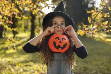 Cadı şapkalı, kıvırcık saçlı, elinde cadılar bayramı portakalı kazanı tutan tatlı bir kız..