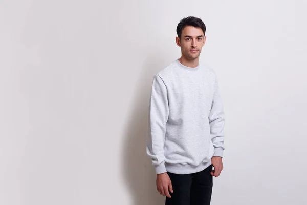 Frontal view of a smiling young brunette man in gray jumper and black jeans isolated white background. — Stock Photo, Image