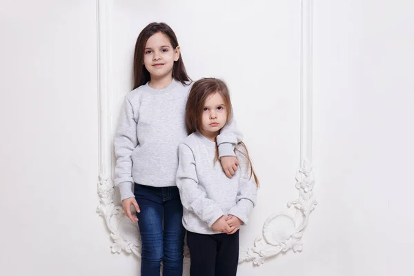 Prachtige twee blanke zusters samen poseren op witte achtergrond, glimlachen en kijken naar de camera. — Stockfoto