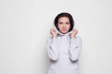Açık gri kazaklı, kapüşonlu esmer bir kadın beyaz arka planda izole edilmiş kameraya bakıyor. Boşluk kopyası.