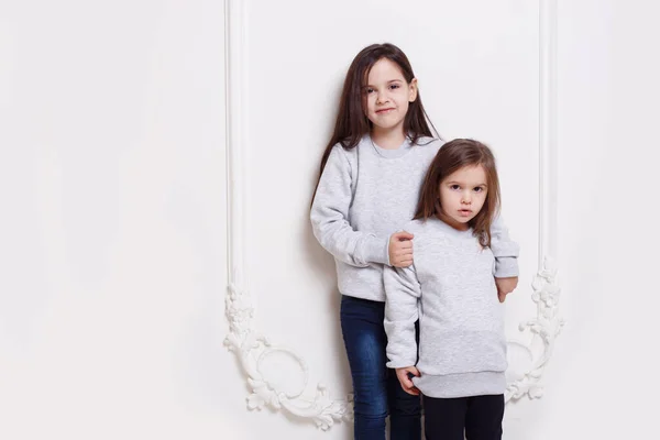 Twee schattige zussen samen poseren op witte achtergrond, glimlachen en kijken naar de camera. — Stockfoto