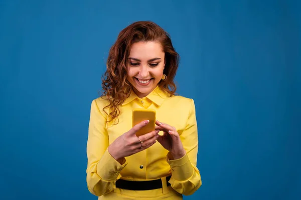 Mavi arka planda akıllı telefonu tutan gülümseyen sıradan bir kadının portresi..