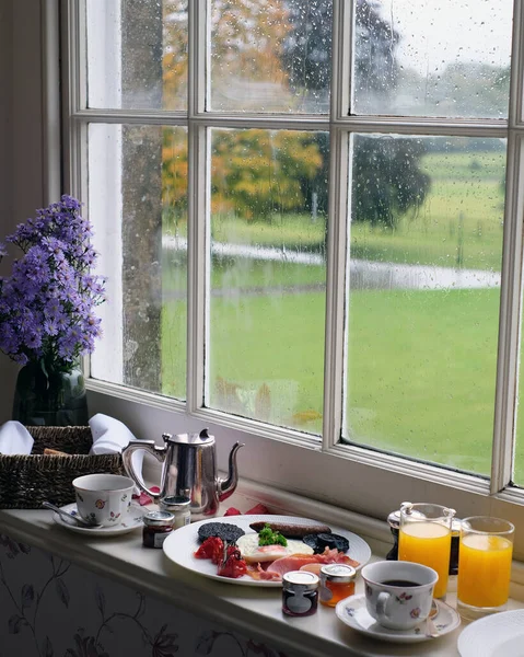 Full English breakfast with tea and coffee by the window on a rainy autumn day in the English countryside hotel