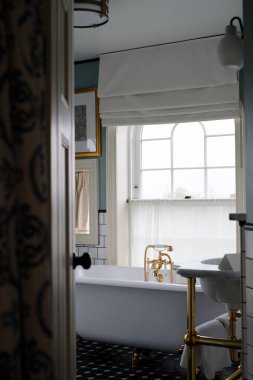 Aydınlık ve güzel antika banyo, eski küveti ve altın musluğu var.