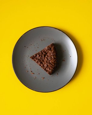 Sarı arka planlı gri tabakta kahverengi kek