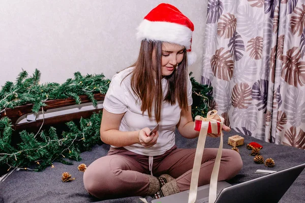 Genç bir esmer kadın dizüstü bilgisayarını elinde tutuyor ve Noel için hediyeler seçiyor..
