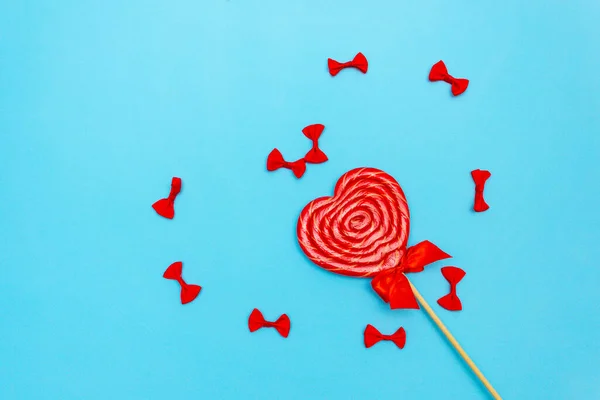 Mavi arka planda fiyonklu lolipop. Yay şeklinde kalp şeklinde. Uzayı kopyala Üst görünüm düzlüğü yalan.