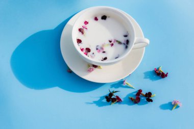 Mavi arka planda vejetaryen sütü ve çiçekli beyaz kupa. Vejetaryen içecek ve yiyecek kavramı, bitki çayı, güzellik ve sağlık, spa.