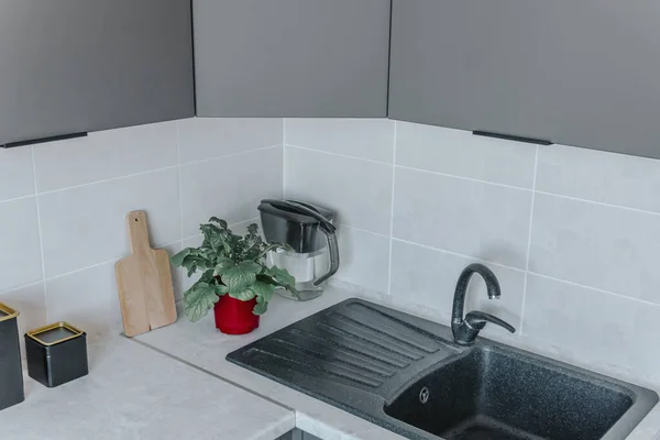 On the kitchen countertop are a chopping board, black containers, and a flower in a red board, next to the sink. The concept of minimalism and environmental friendliness in the kitchen.