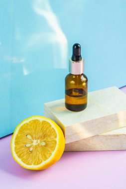 Göz damlası olan bir kozmetik kavanozu podyumlardaki gibi iki granit levhanın üzerinde durur. Arka planda yarım sarı bir limon ve güneşin parıltısının yanında. Yaz için kozmetikler.