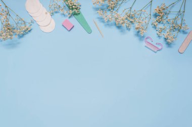 Mavi arkaplandaki manikür aletleri beyaz çigila çiçekleriyle süslenmiştir. Güzellik kavramı. Uzayı kopyala en üstteki görünüm.