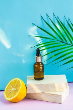 Göz damlası olan bir kozmetik kavanozu, arka planda sarı bir limon, bir palmiye yaprağı ve güneşin parlaklığı gibi iki granit levhanın üzerinde durur. Yaz için kozmetikler.