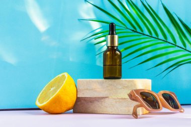 Göz damlası olan bir kozmetik kavanozu iki granit levhanın üzerinde durur, kedi yürüyüşü gibi, yarım sarı bir limon, bir palmiye yaprağı, güneş gözlüğü ve arka plandaki güneşin parlaklığının yanında. Yaz için kozmetikler.