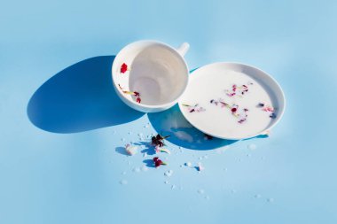 Mavi arka planda bir fincan ile çay tabağında çiçekli süt.